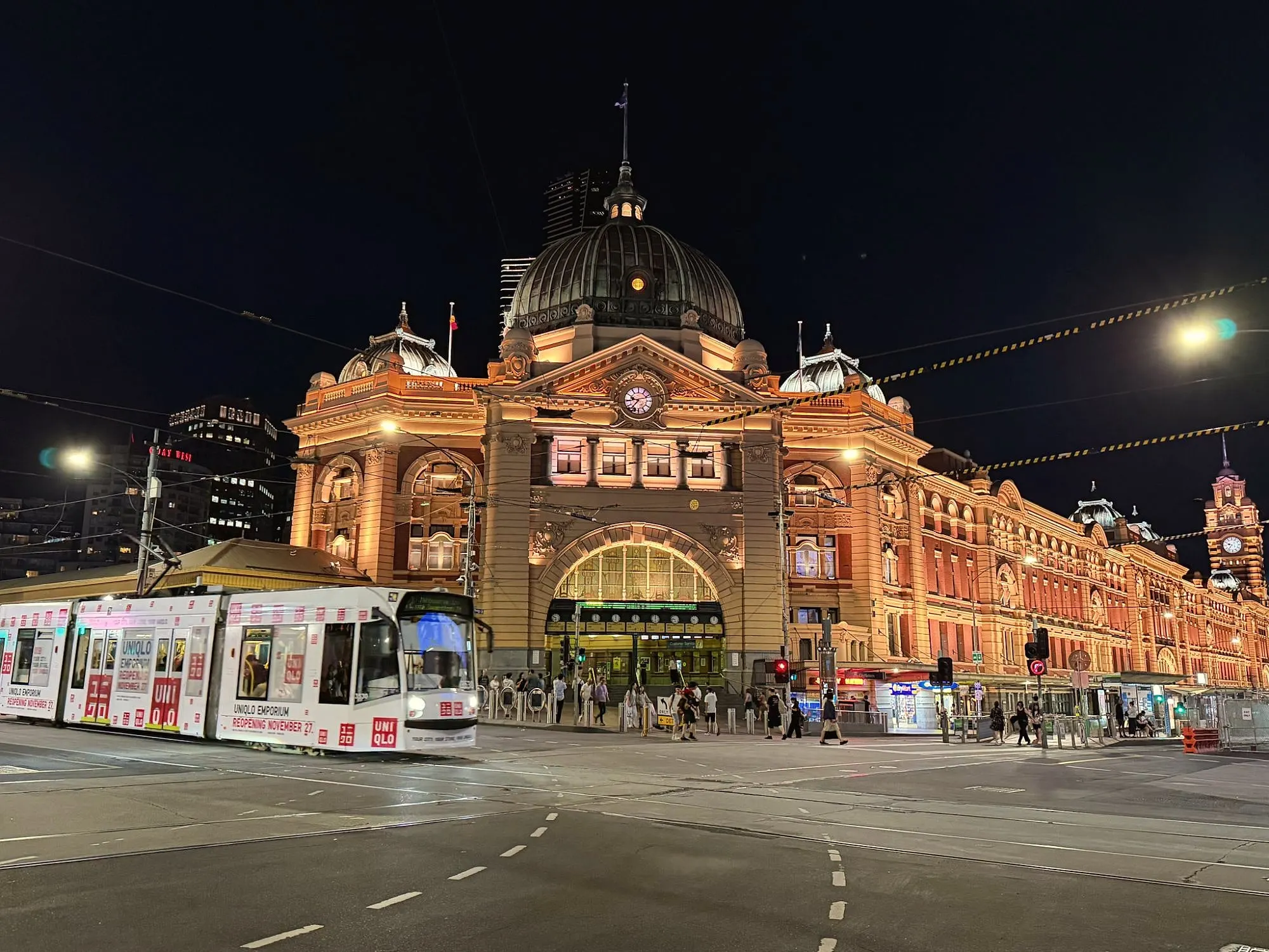 Flinders Street Station lit up at night, with a tram passing in front