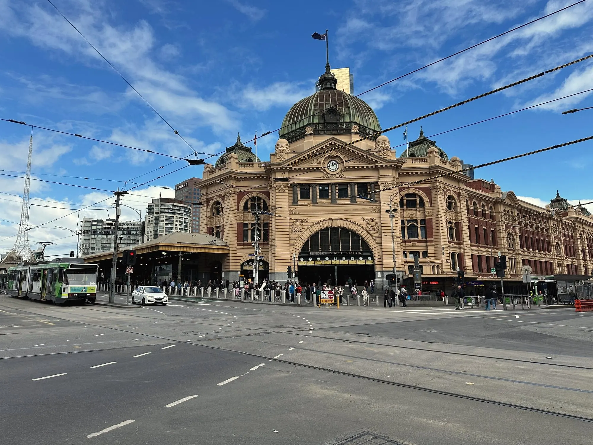 Flinders Street Station with its green dome and row of clocks, a tram passing under a blue sky