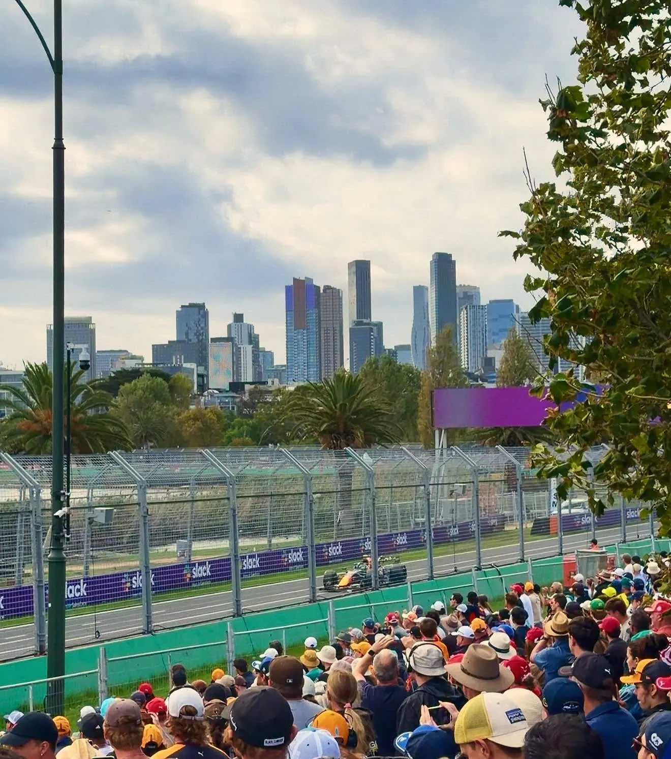 Crowds watching a Formula 1 car on the Albert Park circuit, with the city skyline behind