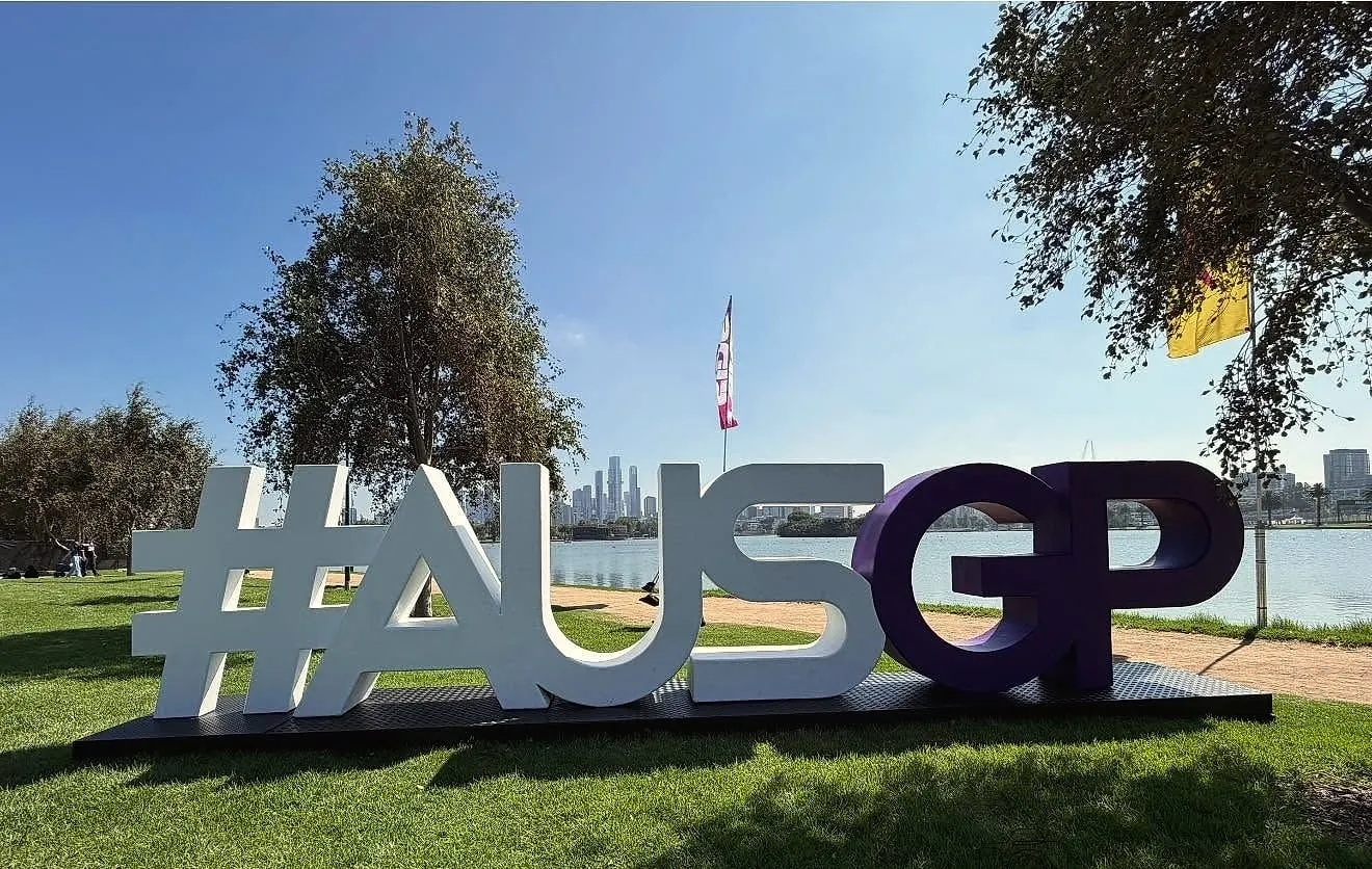 Giant #AUSGP letters on the lawn beside Albert Park Lake, with the city skyline across the water