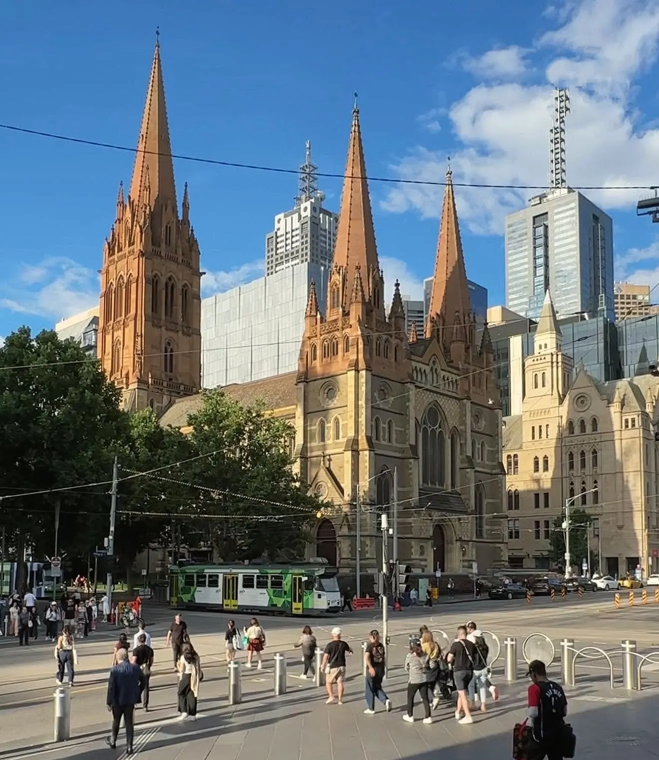 St Paul’s Cathedral in late afternoon sun, seen across the busy corner from Federation Square, with a green tram passing