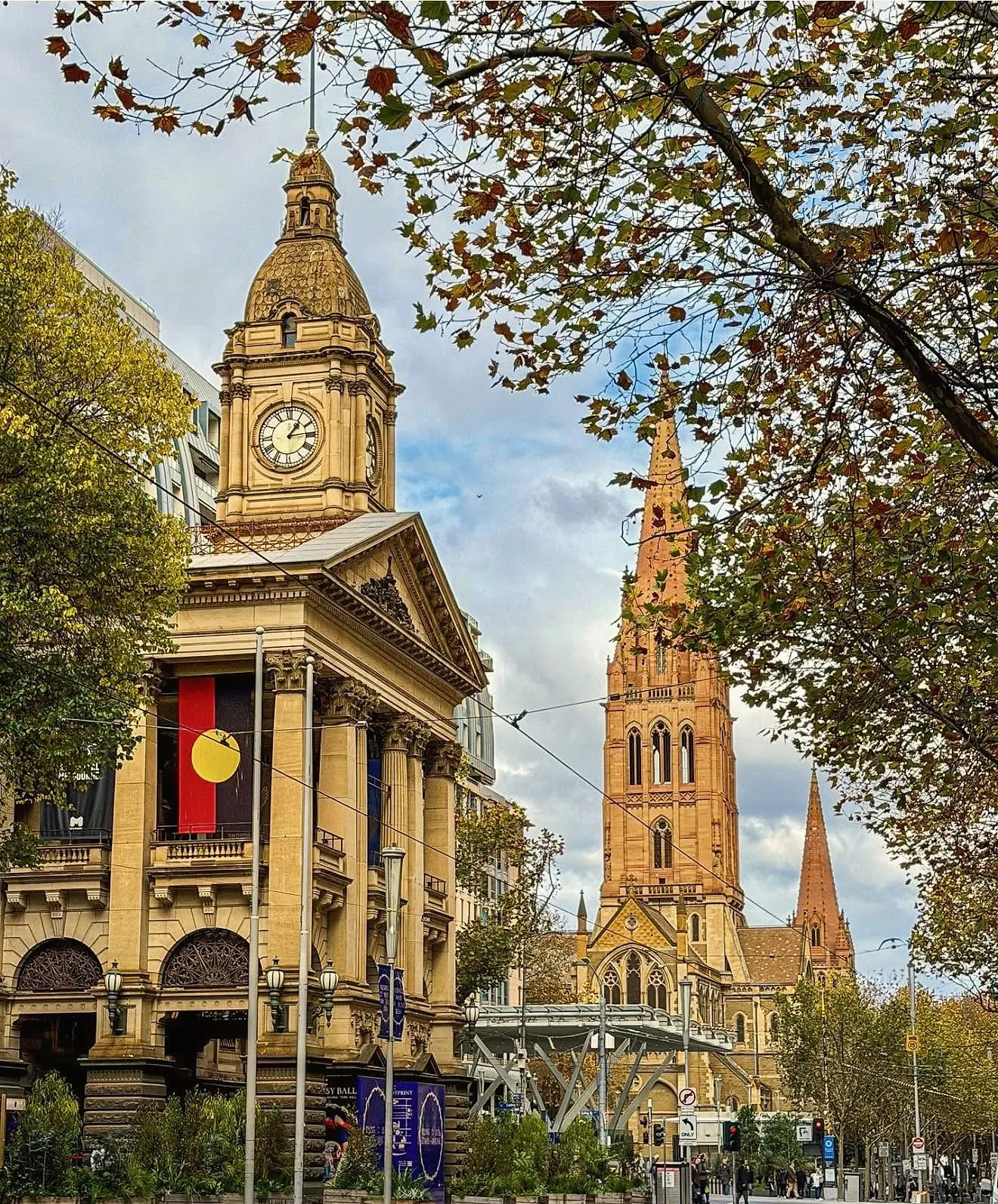 Melbourne Town Hall’s clock tower and St Paul’s spires along Swanston Street, framed by autumn leaves