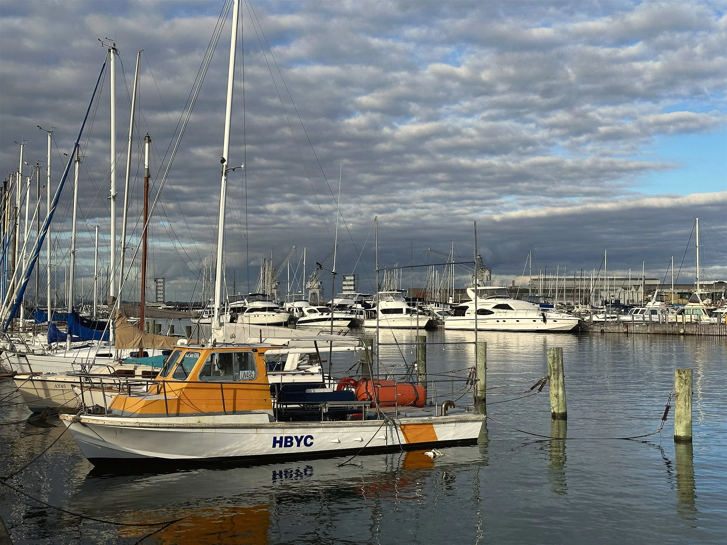 A yellow and white boat moored among yachts beneath a grey, rippled sky